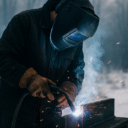 Soudeur en action par temps froid, portant une combinaison de protection et un casque, avec des étincelles illuminant l’air hivernal